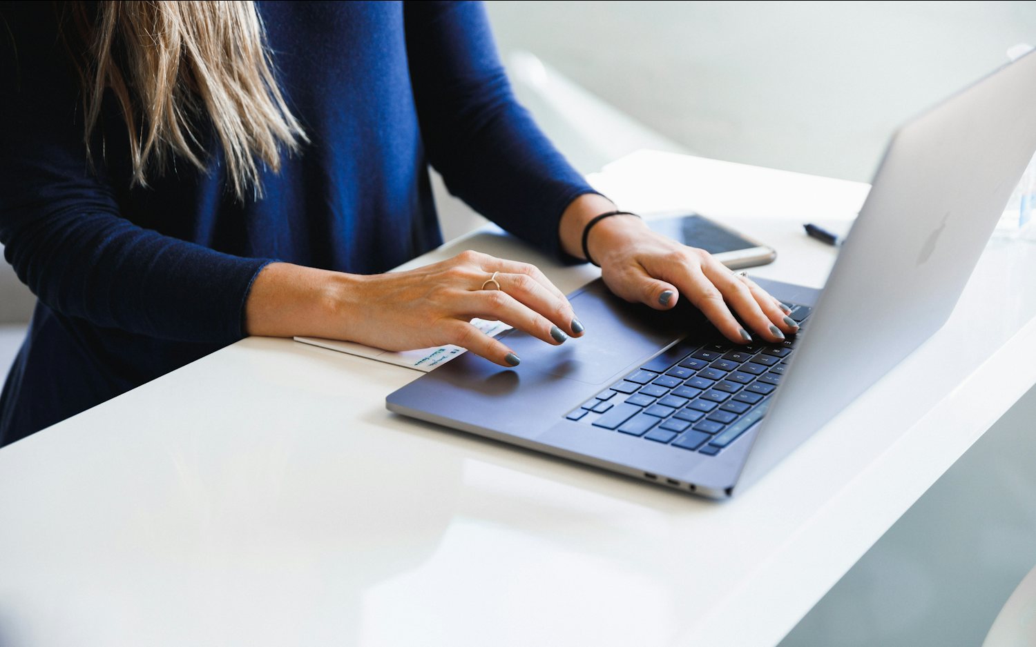 A woman in a blue long-sleeve shirt working on a laptop