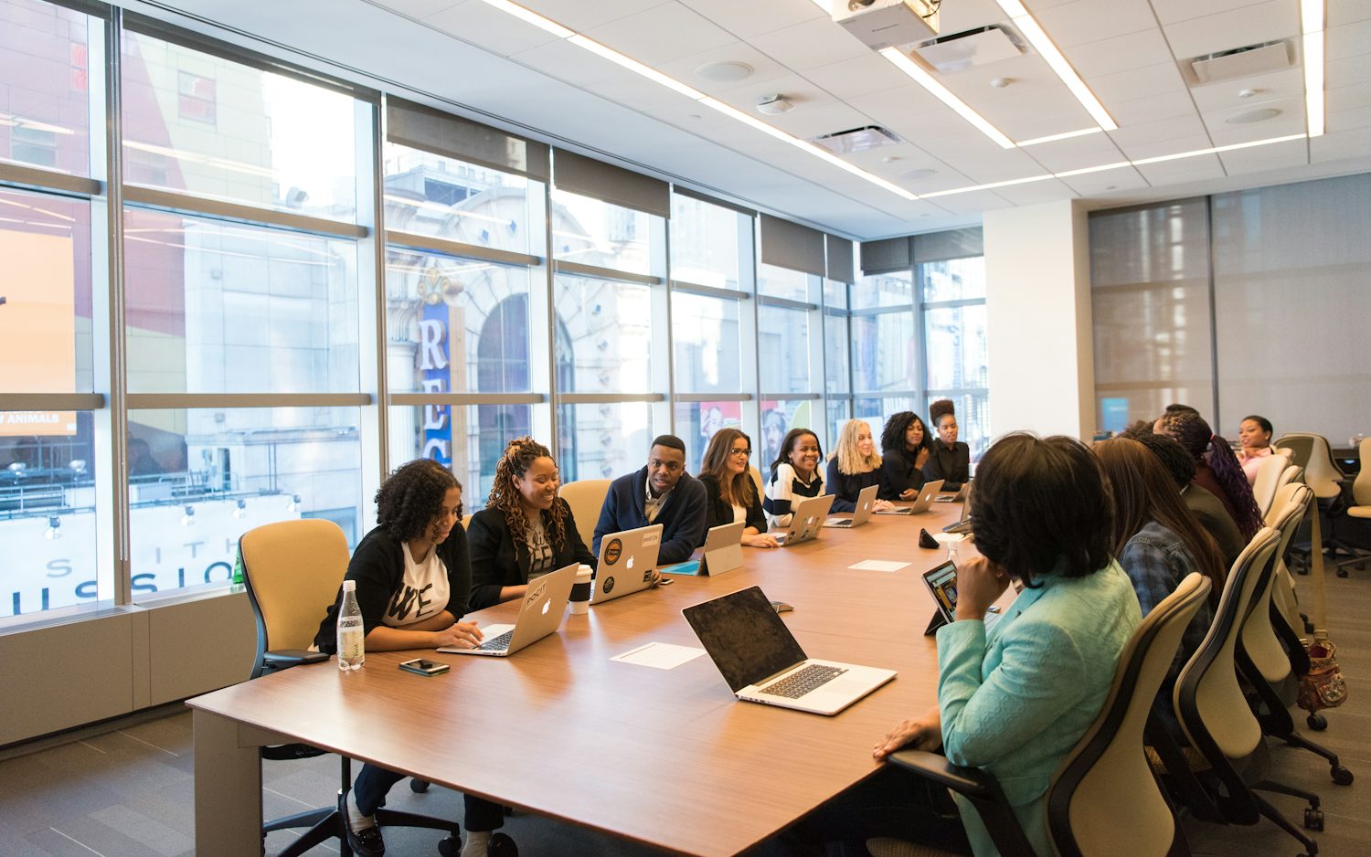 A group of people sitting around a wooden table with laptops