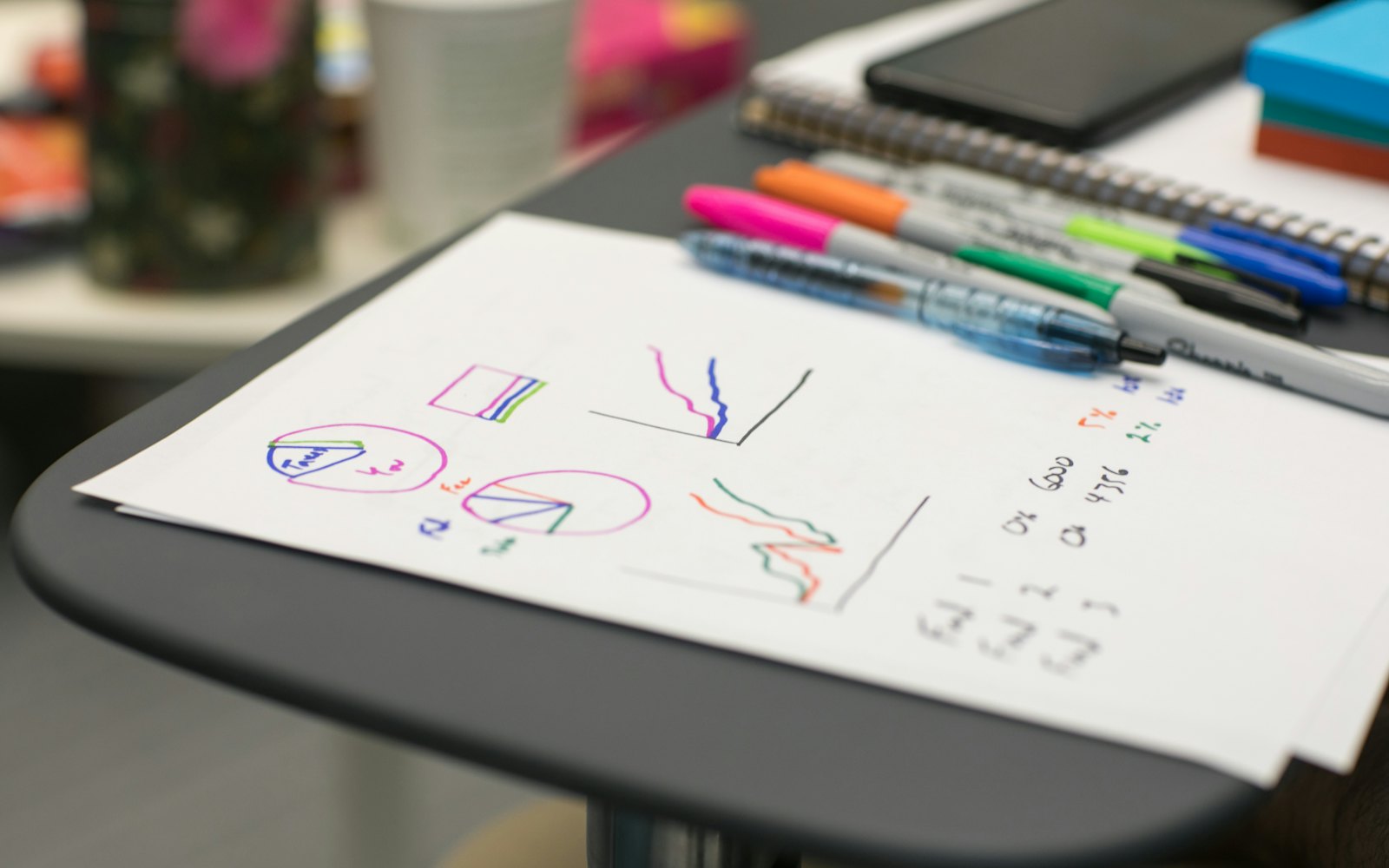 Rough marker sketches on a sheet of white paper with a row of colored markers lying beside it