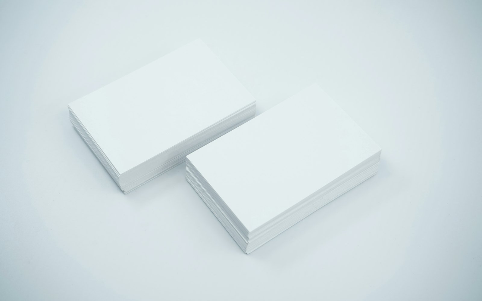 Two stacks of blank white business cards on a pale gray surface