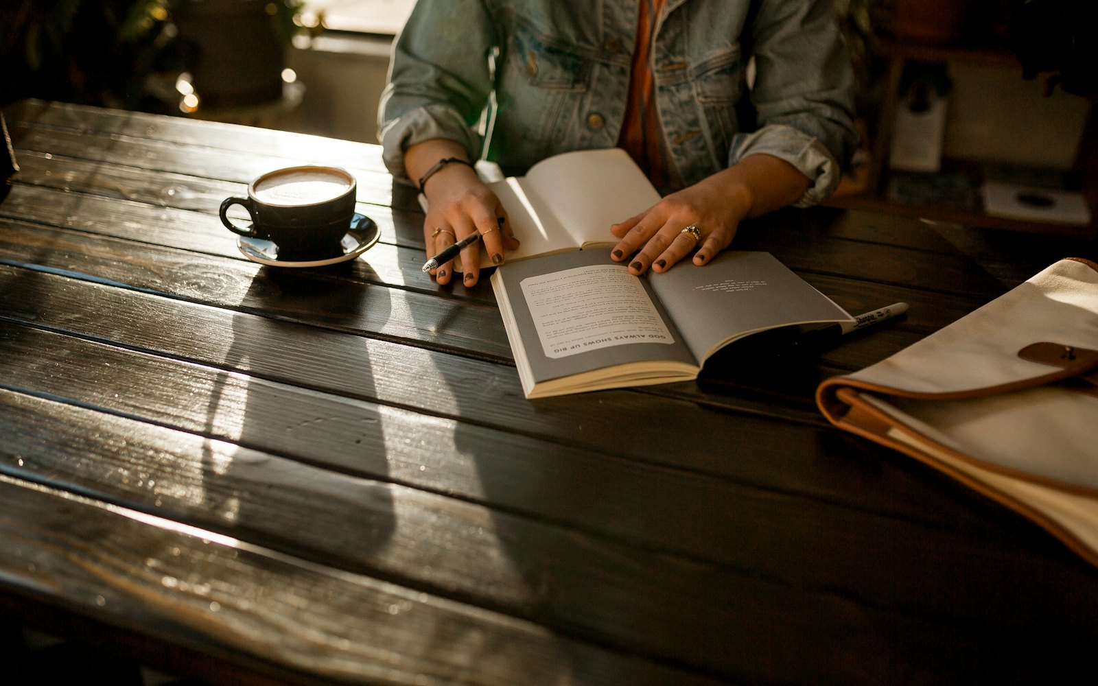 Hands holding a pen over an open notebook on a dark wooden table beside a cup of coffee