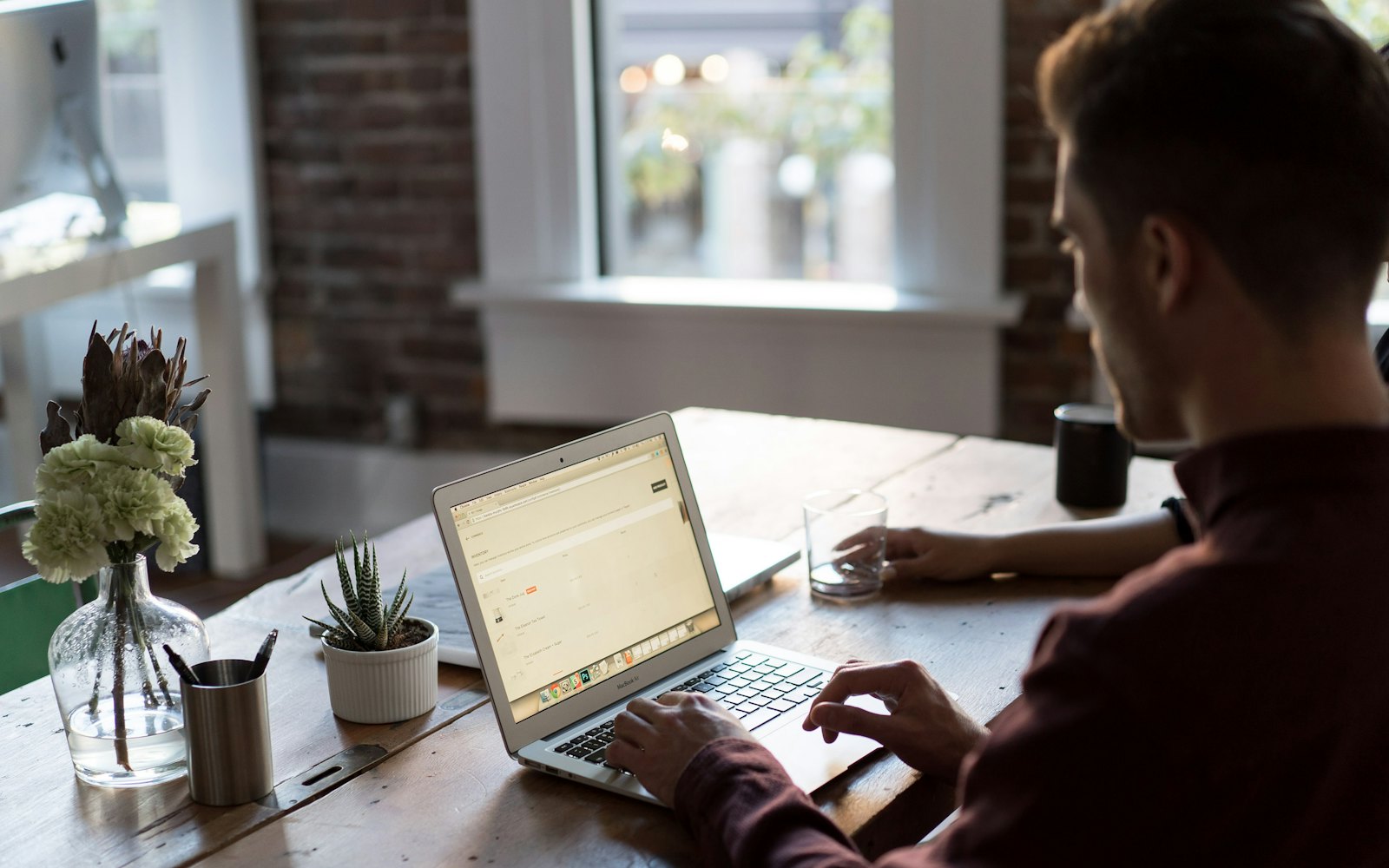 A founder working on a laptop at a wooden table beside a brick wall