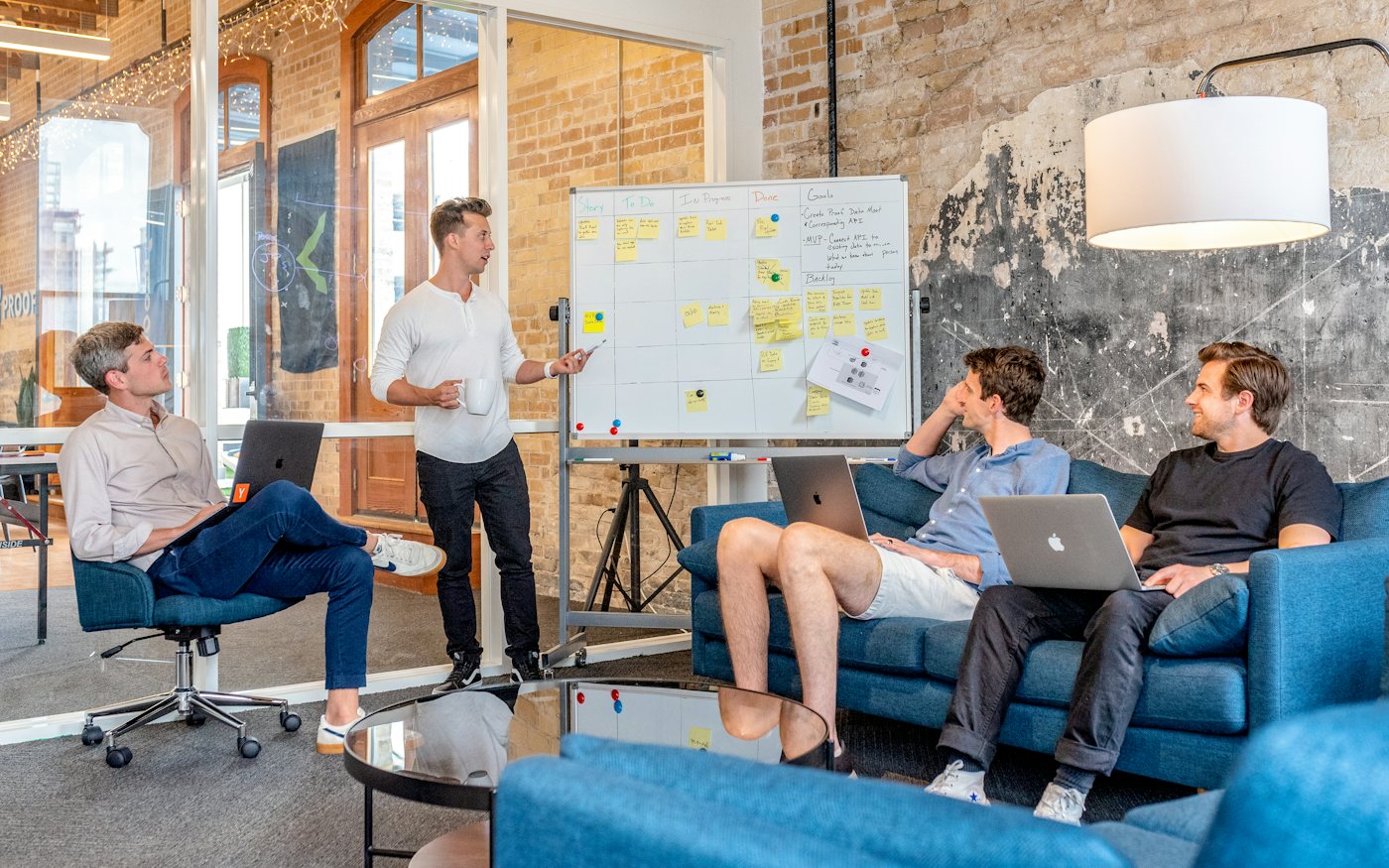 A small founding team with laptops listening to a teammate at a whiteboard