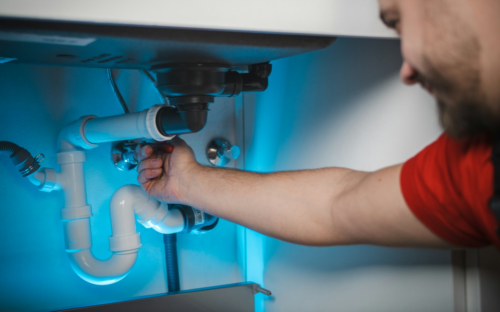 A plumber tightening a fitting on the pipes under a sink