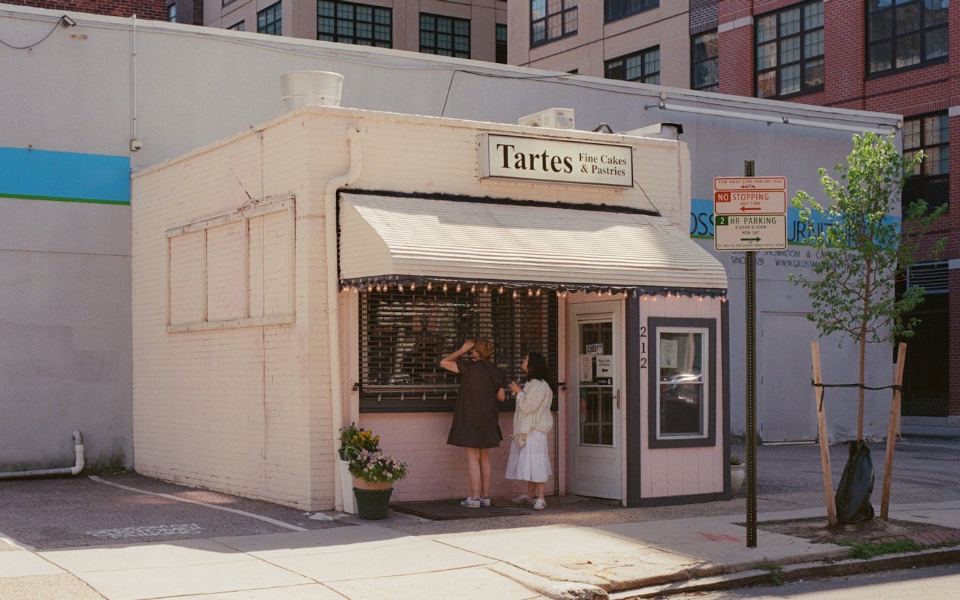 Two customers standing outside a small neighborhood bakery storefront with an awning