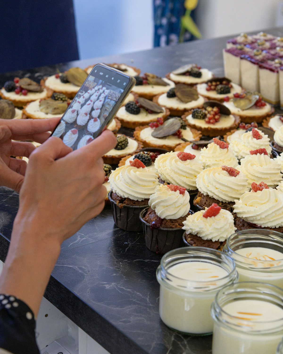 A woman photographing cupcakes on a table with a phone