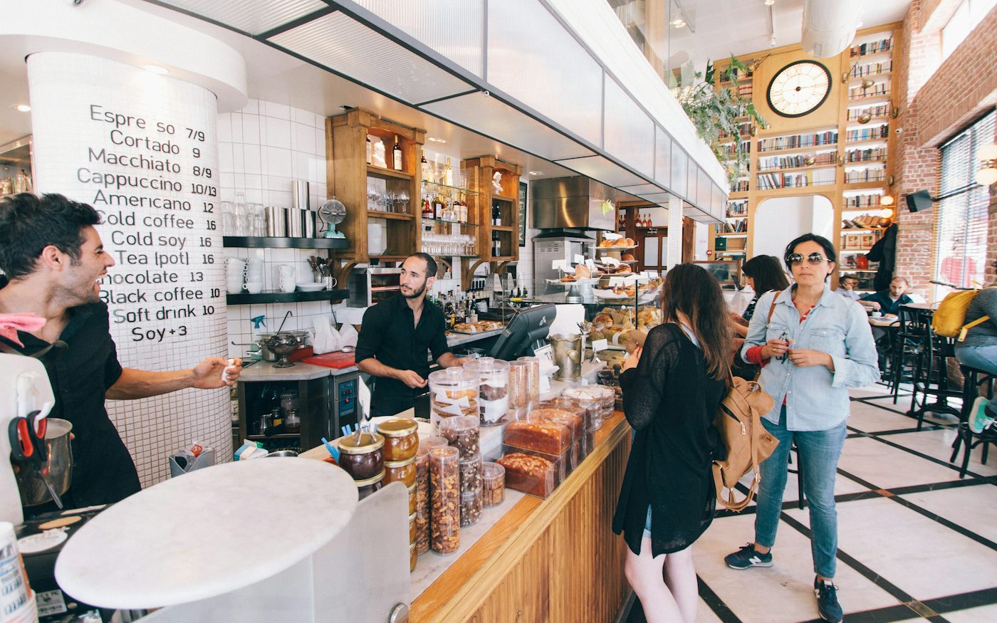 A busy coffee shop with staff behind a wooden counter and customers standing in line