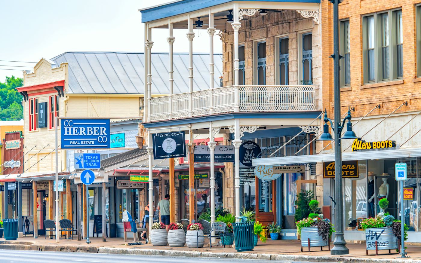 A row of historic stone and brick storefronts with hanging shop signs along a small-town main street