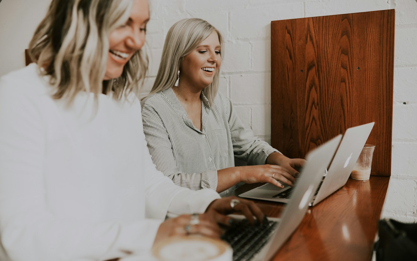 Two women laughing together over laptops at a wooden counter