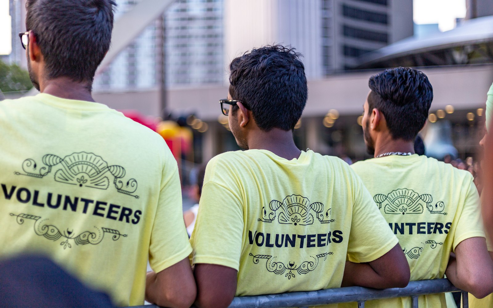 Three volunteers in yellow Volunteers shirts watching a crowd at an outdoor city event
