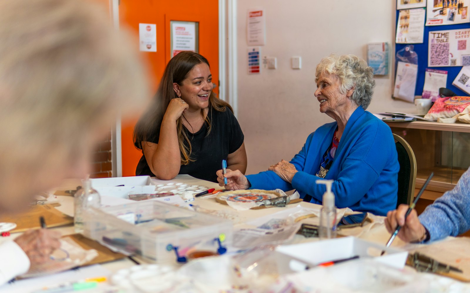 A younger and an older woman talking at a table during a community art class