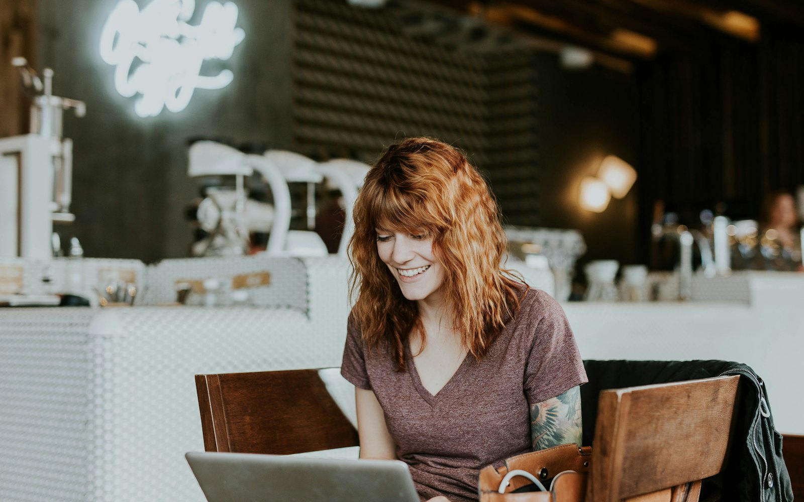 A woman smiling at her laptop at a table in a coffee shop