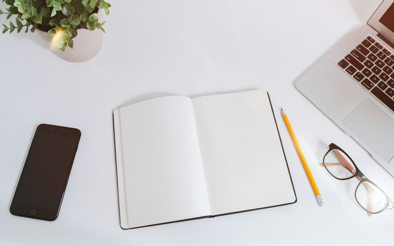An open notebook beside a phone and laptop on a white desk
