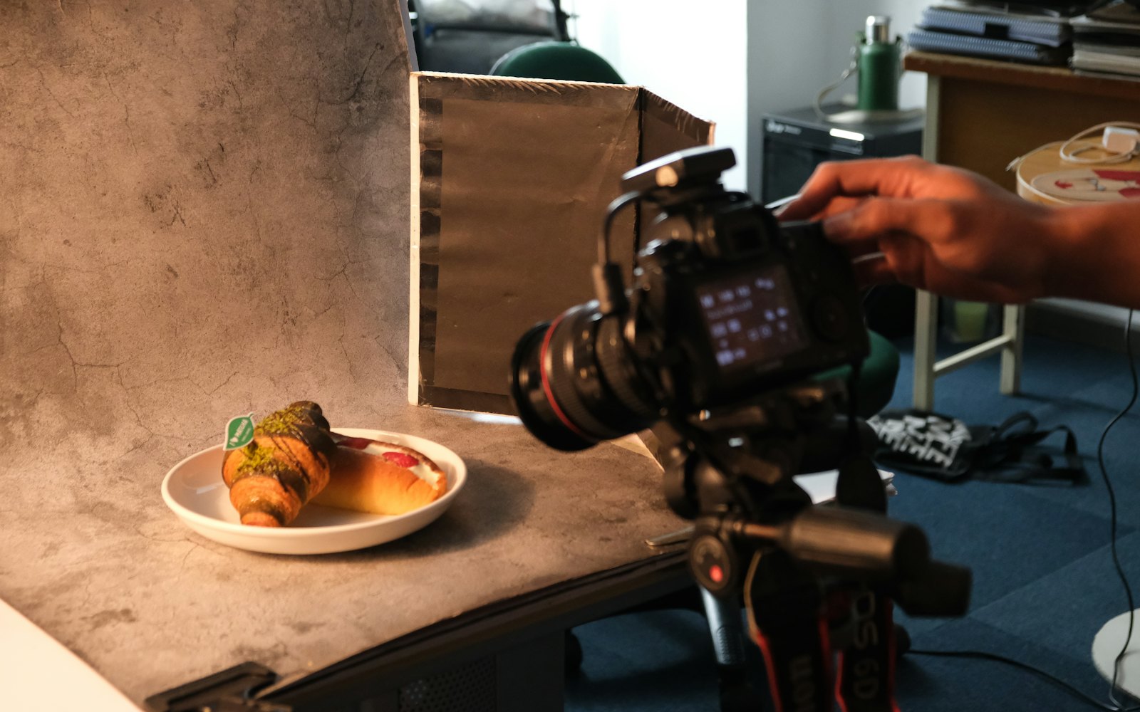 A camera on a tripod photographing two pastries on a plate against a gray backdrop